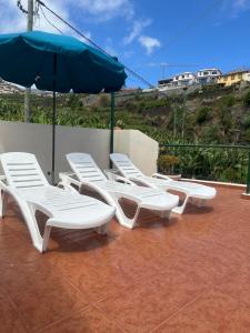 four white chairs and an umbrella on a patio at Elisabeth House in Ponta do Sol