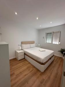 Claveles de Luxe في مالقة: غرفة نوم بيضاء مع سرير وأرضية خشبية