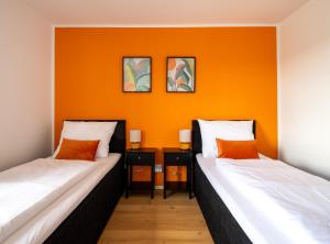 two beds in a room with an orange wall at C4S -COME4STAY- Stilvoll eingerichtetes Apartment für bis zu 8 Personen - Hochwertige Betten I voll ausgestattete Küche I Balkon I Badezimmer I WLAN I Smart TV in Töging am Inn