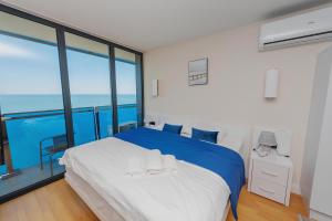 Schlafzimmer mit einem blauen und weißen Bett und einem großen Fenster in der Unterkunft Orbi City apartment with sea view in Batumi