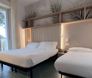 two beds in a hotel room with white sheets at Pinetina Mare Baby Family Hotel in Cervia