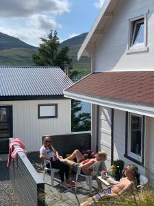 three women sitting in chairs on a porch of a house at Fjordcottage in Søldarfjørður