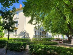 a large white building with trees in front of it at Tornyai Apartman in Hódmezővásárhely