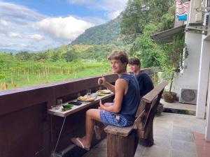 deux jeunes hommes assis à une table et mangeant de la nourriture sur un balcon dans l'établissement Pimpa House, à Ban Hua Nam Mae Sakut