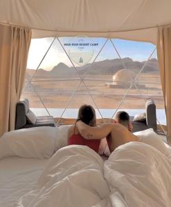 un hombre y una mujer acostados en la cama mirando por la ventana en Wadi Rum desert camp, en Wadi Rum