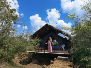 Una mujer parada en el porche de una cabaña de paja en Basecamp - Yala, en Yala