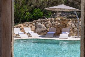 eine Gruppe Stühle und ein Sonnenschirm neben einem Pool in der Unterkunft Villa Pevero Porto Cervo in Porto Cervo