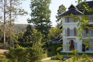 uma antiga casa branca com árvores em primeiro plano em Sela Chiangmai em Chiang Mai