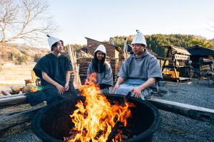 grupa trzech osób siedzących przy ogniu w obiekcie サウナ付き古民家宿まるもり w mieście Wada