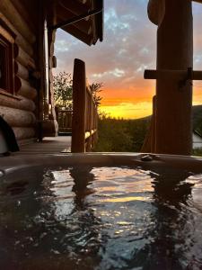 bañera de hidromasaje en un porche con puesta de sol al fondo en Böhmerwald Lodges en Ulrichsberg