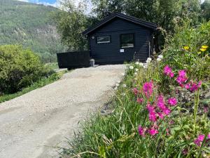 eine schwarze Hütte auf einem Feldweg neben Blumen in der Unterkunft Koselig gårdshus in To