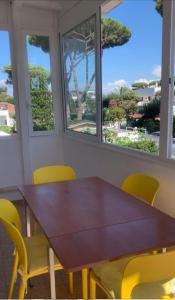 a wooden table and yellow chairs in a room with windows at Casa di Clara Fregene in Fregene