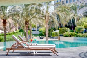 um par de cadeiras sentadas ao lado de uma piscina com palmeiras em Crowne Plaza Muscat OCEC, an IHG Hotel em Mascate