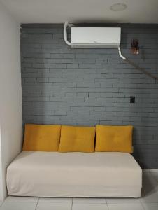 a bed with three yellow pillows against a brick wall at La Playa Hospedagem in João Pessoa