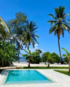 a swimming pool next to a beach with palm trees at Lions Zanzibar SUITE&APARTEMENT with private pool - LUXURY ON THE SEASIDE in Bunju