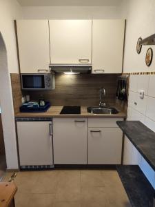 cocina con armarios blancos, fregadero y microondas en Apartmenthaus Bader, en Leutasch