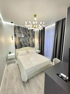 Un dormitorio con una cama blanca y una lámpara de araña. en Lux апартаменты в новом центре Караганды, en Karagandá