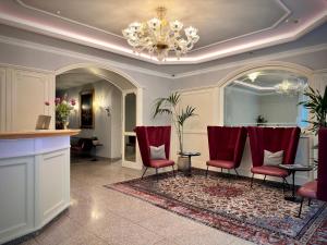 una sala de espera con sillas rojas y una lámpara de araña en Windsor Merano Hotel & Suites, en Merano