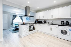 cocina con armarios blancos, lavadora y secadora en Dartford, Kent - Modern 2Bd 2Bath En-Suite Bungalow M25 Bluewater en Dartford