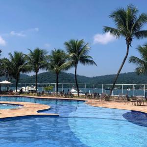 una gran piscina con palmeras y el océano en Apartamento no Hotel Porto Marina Mangaratiba, en Mangaratiba