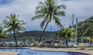 una piscina con sillas y palmeras junto a un puerto deportivo en Apartamento no Hotel Porto Marina Mangaratiba, en Mangaratiba