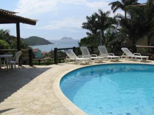 a swimming pool with lounge chairs and the ocean at BUZIOS PRAIA PISCINA ePOR doSOL noMar in Búzios