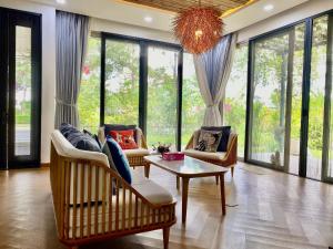 a living room with chairs and a table and windows at Green villa in Bien Hoa