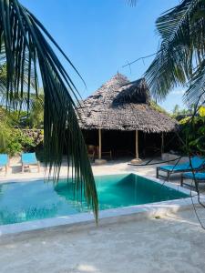 a resort with a swimming pool and a thatch hut at Sand Beach Boutique Villas in Bwejuu