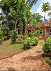 a red house with palm trees and a dirt road at Royalstar Resort in Vagator