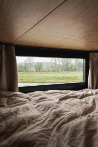 Bett mit Blick auf ein Feld durch ein Fenster in der Unterkunft Ekko tiny house in Philippeville