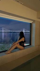 a woman sitting on a window sill looking out at a bridge at Paradise on earth in Busan