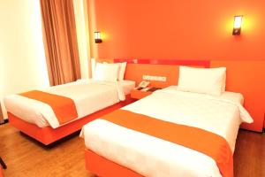 2 camas en una habitación de hotel con paredes de color naranja en Halogen Hotel Airport Surabaya, en Sidoarjo