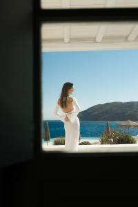 a woman in a wedding dress standing in front of the ocean at Mykonos Pantheon in Kalo Livadi