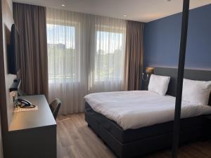ホーフトドルプにあるOZO Hotels Antares Airportのベッド、デスク、窓が備わるホテルルームです。