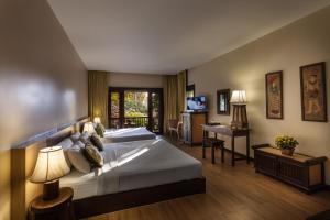 a bedroom with a bed and a desk with a television at Lanna Dusita Riverside Boutique Resort in Chiang Mai