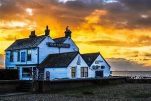 ein Gebäude am Strand mit einem Sonnenuntergang im Hintergrund in der Unterkunft The Salty Mermaid Fisherman's Cottage, Whitstable in Kent