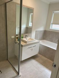 a bathroom with a sink and a mirror and a tub at KozyGuru Greenvale 5 Bedroom Holiday Home in Greenvale