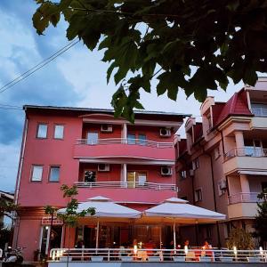 różowy budynek ze stołami i parasolami przed nim w obiekcie Villa Rimari w Ochrydzie