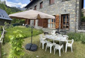 a table with white chairs and an umbrella in a yard at Rincón de Bachatos Casa Rural in Piedrafita de Jaca