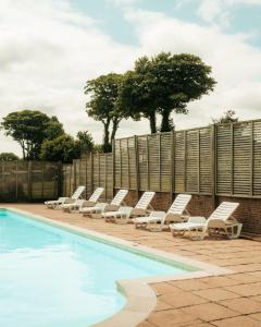 a row of lounge chairs next to a swimming pool at Hot Tub Lodge Cornwall - Meadow Lakes Holiday Park in St Austell