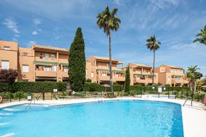 ein Swimmingpool mit Palmen und Gebäuden in der Unterkunft Jardín del Golf apartamento con jardín privado in Chiclana de la Frontera