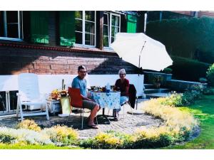 un homme et une femme assis à une table sous un parapluie dans l'établissement Apartment Träumli by Interhome, à Lenk im Simmental