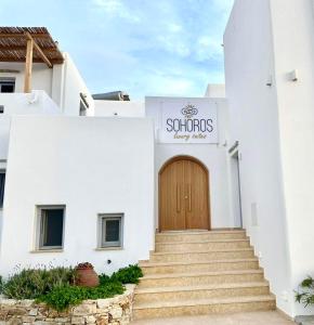 een wit gebouw met een houten deur en trap bij SOHOROS suites in Skhoinoussa