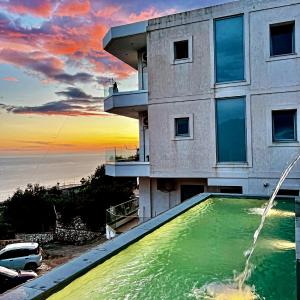 a building with a swimming pool in front of a sunset at Ionian Pearl in Dhërmi