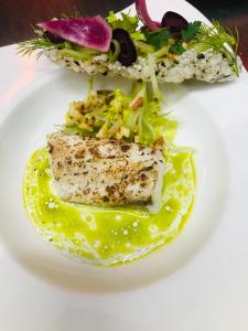 un piatto bianco con un pezzo di pesce e un'insalata di STAG & THISTLE HOTEL AND RESTAURANT a Fraserburgh