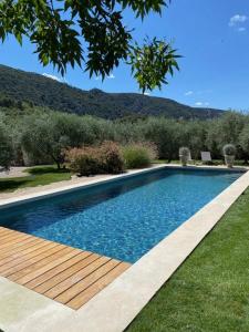 a swimming pool with a wooden deck next to a yard at Le Champ des Oliviers in Oppède