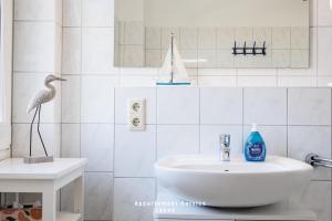 Un baño blanco con un lavabo y un pájaro en la encimera. en Hafenresidenz Fördeglück, en Laboe 19 fotos más