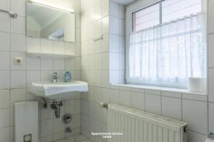 a white tiled bathroom with a sink and a window at Kapitänshaus W13 in Laboe