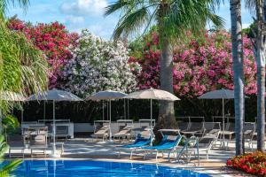 una piscina del resort con sedie, ombrelloni e fiori di Oleandri Resort Paestum a Paestum