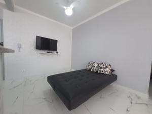 un sofá negro en una habitación blanca con TV en BEIRA MAR I - TUPI - 15 metros da praia - 2 dormitórios com VARANDA - WI FI e acomoda até 8 pessoas - ESTACIONAMENTO Gratuito en Praia Grande
